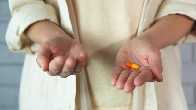 Person opening hands revealing two different pills. Close-up view of a person wearing a tunic, slowly opening their hands to reveal a blue and a yellow pill, representing a difficult medical choice