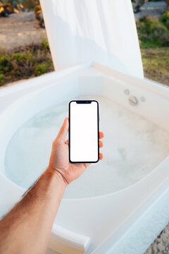 Hand Holds a Phone With White Screen Above a Hot Tub