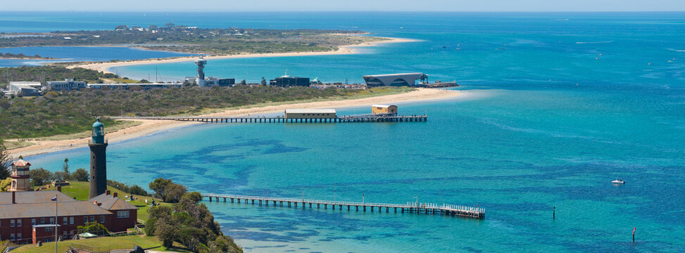 A lighthouse on a coastal cliff in front of jettys on a calm ocean bay