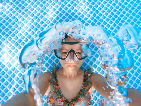 Girl taking a self portrait in a pool while blowing air bubbles