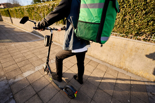 Food courier riding electric scooter delivering meal in city