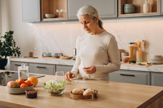 Positive old woman takes capsule from pill organizer cell on table