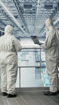 Vertical video Employees in safety suits reviewing microchip smart factory schematics, talking. Teamworking colleagues collaborating, overseeing gear layouts using EDA software in industry 4.0 plant
