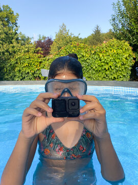 Girl having fun in a pool with action camera looking at the recordings