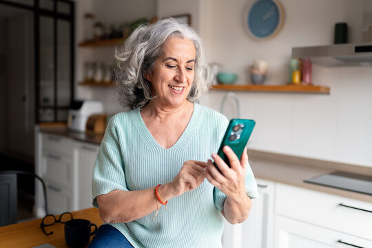 Senior woman smiling using smartphone in kitchen