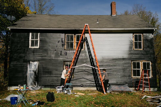 young men  moving ladder to paint siding of old 1787 house