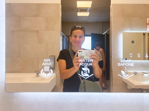 Woman taking a bathroom mirror selfie at a restaurant with her phone.