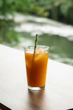 Refreshing orange juice with ice and straw near a river