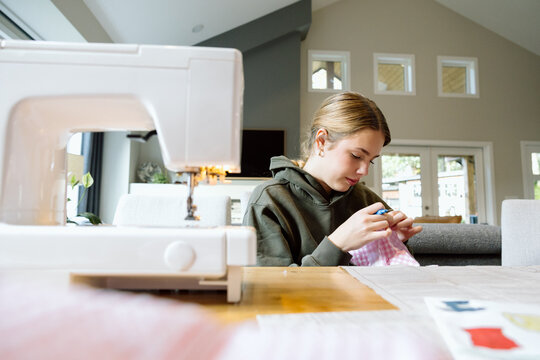 Teen girl sewing at home with a sewing machine, candid hobby