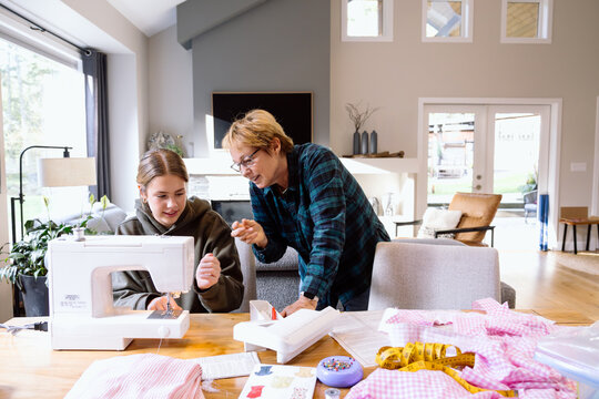 Grandmother teaching girl to sew at home, family moment