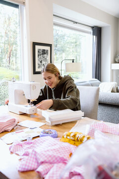 Candid teen sewing at home with sewing machine and fabric