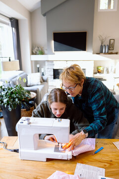 Grandmother teaching granddaughter to sew at home