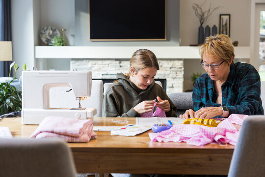 Candid grandmother teaching granddaughter to sew at home