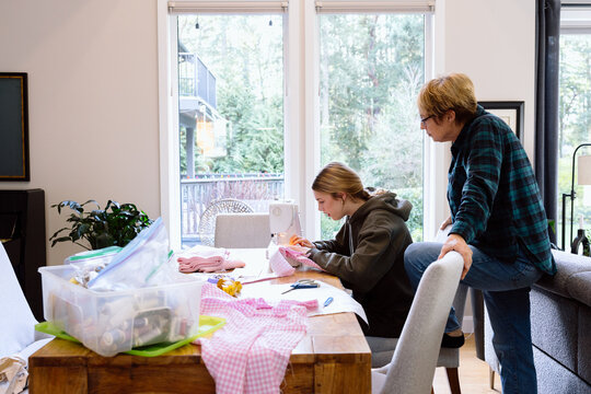 Grandmother teaching granddaughter to sew at home table