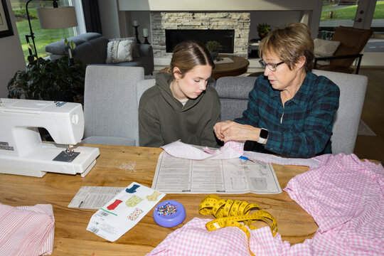 Candid grandmother teaching granddaughter to sew at home