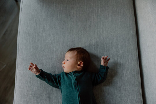 Candid newborn baby lying on gray couch looking to the side
