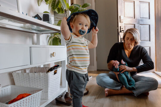 Toddler wearing hat stands while mother cares for newborn at hom