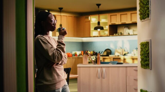 African american peaceful woman enjoying warm drink at the house, enjoying tea time with a reflective attitude. Young adult relaxing at home with soft light, serene natural peace.
