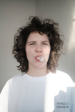 Young woman blows bubblegum in bright indoor setting