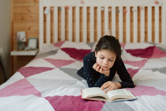 Girl in her room lying on the bed and reading a book. 