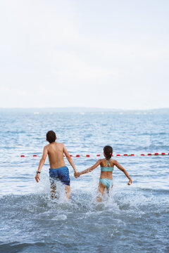 Siblings running into the sea. They are carefree and happy. 