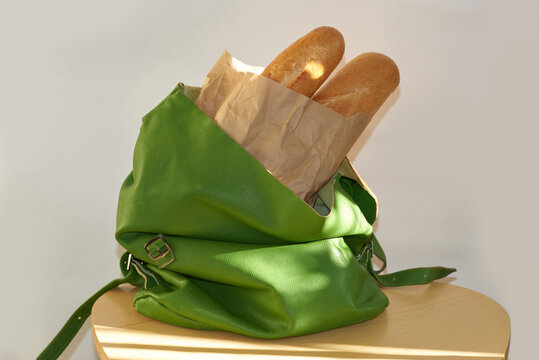 Brown bread sticks are placed in a green backpack on a wooden table
