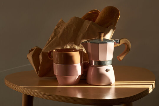 Dark brown paper bag with bread, two cups and a moka pot