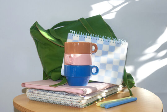 Bright cups and notebooks are on the table next to green backpack