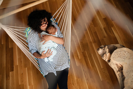 Mother Cuddling Newborn Baby In Indoor Hammock