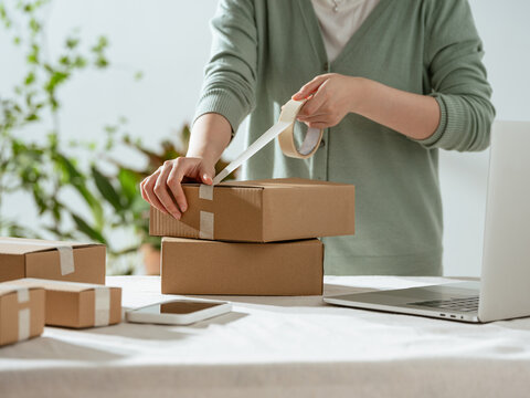 Hands taping up cardboard boxes for shipping, preparing online orders