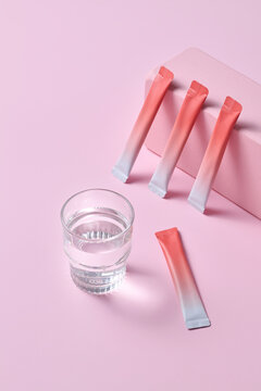 Wellness Drink Sachets and Glass of Water on Pink Background