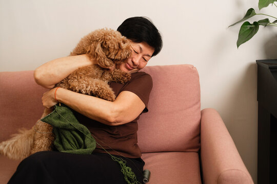 Woman enjoys time with dog on couch while knitting