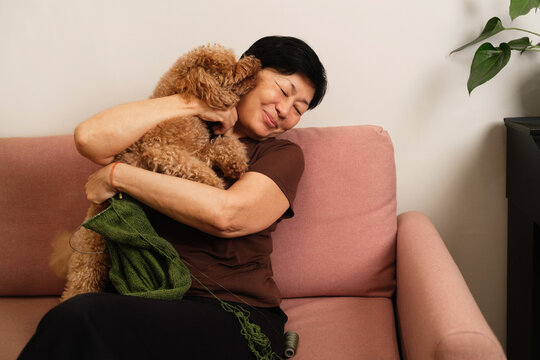 Woman enjoys time with dog on couch while knitting