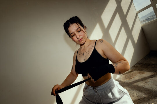 Female boxer sitting in a gym, wrapping her hands before training.
