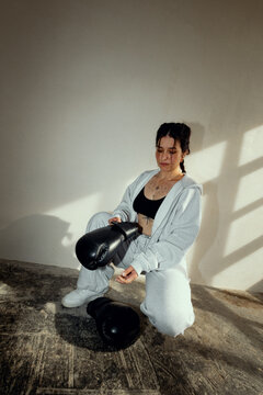 boxer squatting against a white wall, putting on her boxing gloves