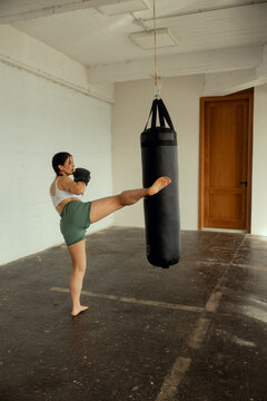 Female boxer delivering a kick to a punching bag during training.