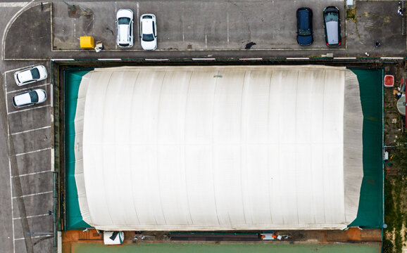 Aerial view of a large white tensile structure and a parking lot with parked cars in Reggello, Tuscany, Italy.
