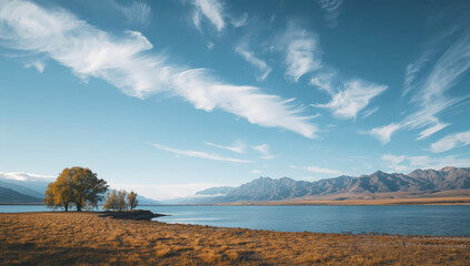 Naklejka premium Golden lakeside tree cluster with sweeping clouds and distant mountain range