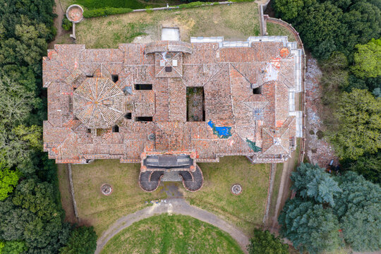 Aerial view of the historic Sammezzano Castle with its intricate terracotta rooftops and octagonal tower surrounded by lush green forest in Reggello, Tuscany, Italy.