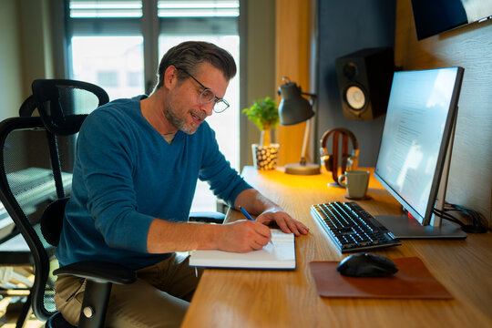 Man writes in a notebook at a home office desk
