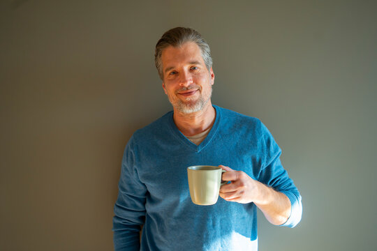 Man enjoys coffee while standing by a wall