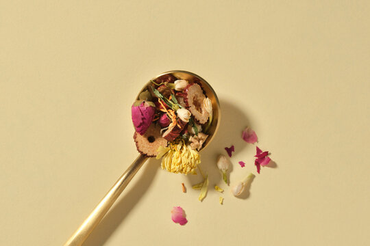 A golden spoon cradles a mix of dried herbs and flowers