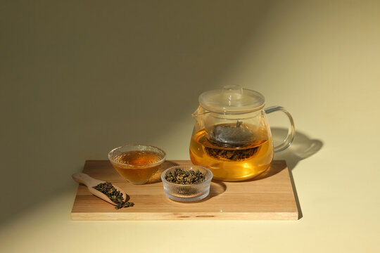 A glass teapot brewing tea, complemented by tea leaves and a bowl