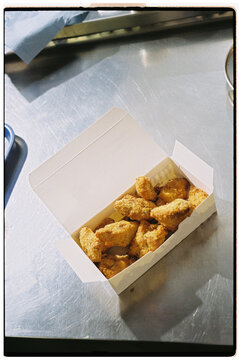 Takeout box with chicken nuggets on a stainless steel counter
