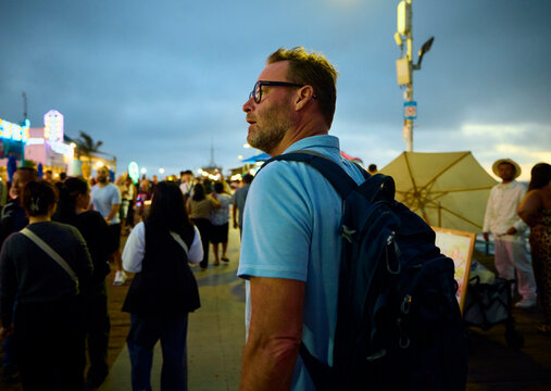 A man strolls along a bustling pier in Santa Monica as dusk falls.
