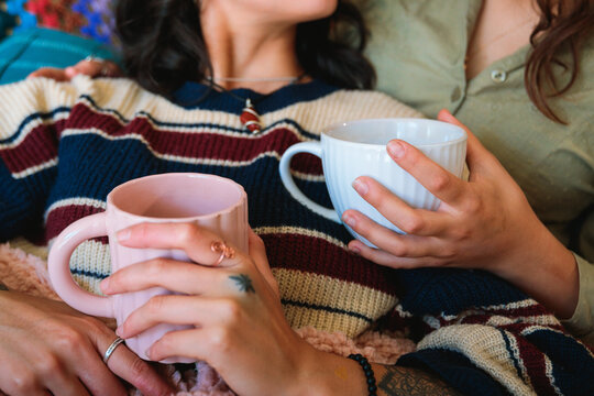 Couple Holding Warm Drinks While Relaxing on Sofa
