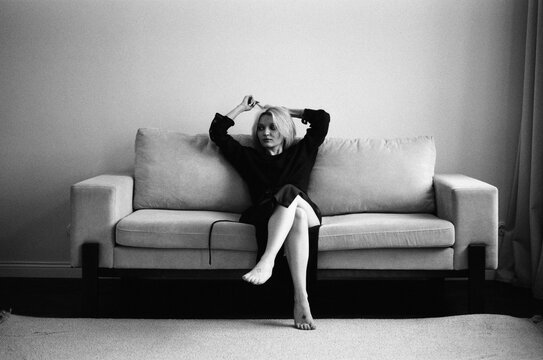 Barefoot Blonde Fixing Hair on Sofa, B&W Film Portrait