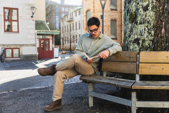 Thoughtful Young Man Reading a Book on a Wooden Bench