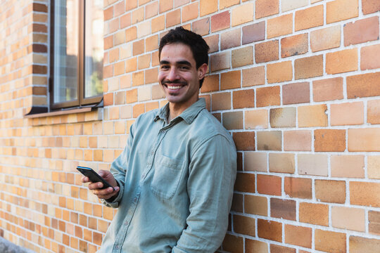 Man Leaning Against Brick Wall Using Smartphone Outdoors