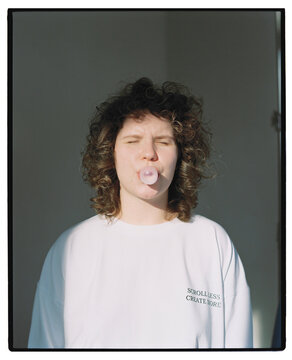 Woman blows bubble gum in a bright room with plain walls